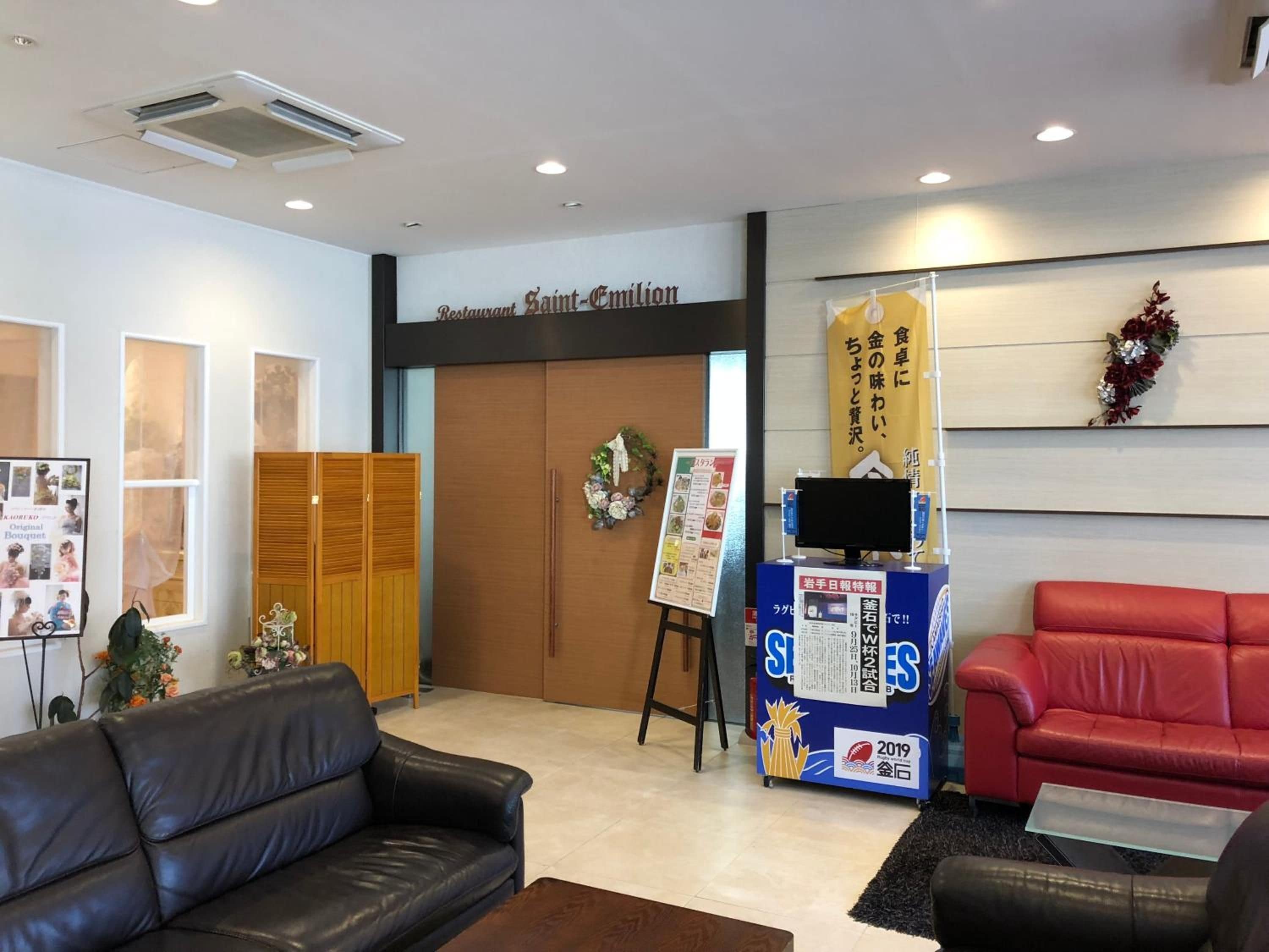 A reception area with a black leather couch, a red sofa, a wooden cabinet, and a wall-mounted TV.