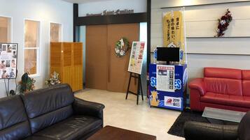 A reception area with a black leather couch, a red sofa, a wooden cabinet, and a wall-mounted TV.