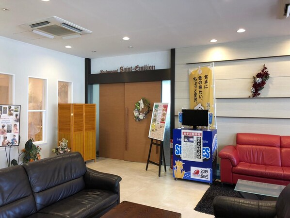 A reception area with a black leather couch, a red sofa, a wooden cabinet, and a wall-mounted TV.