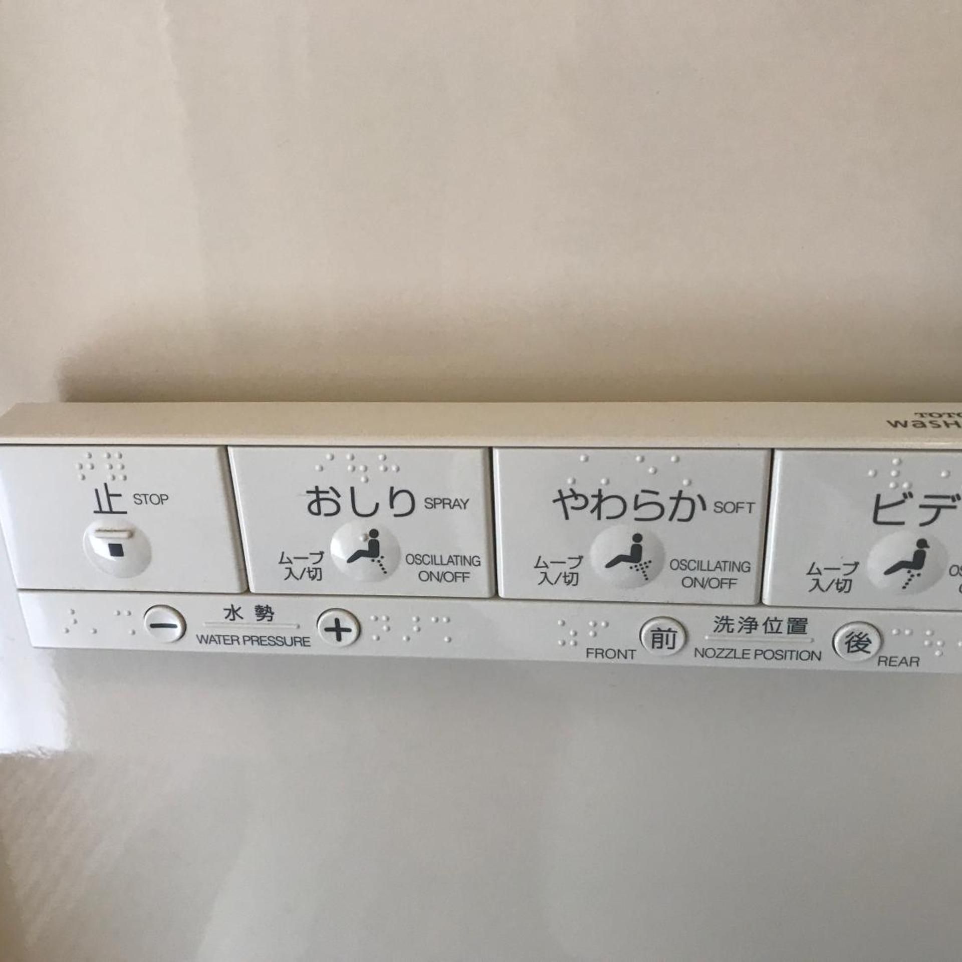 Panel de control con etiquetas en japonés para las funciones detener, rociar, suave y trasero, junto con controles de presión del agua y posición de la boquilla.