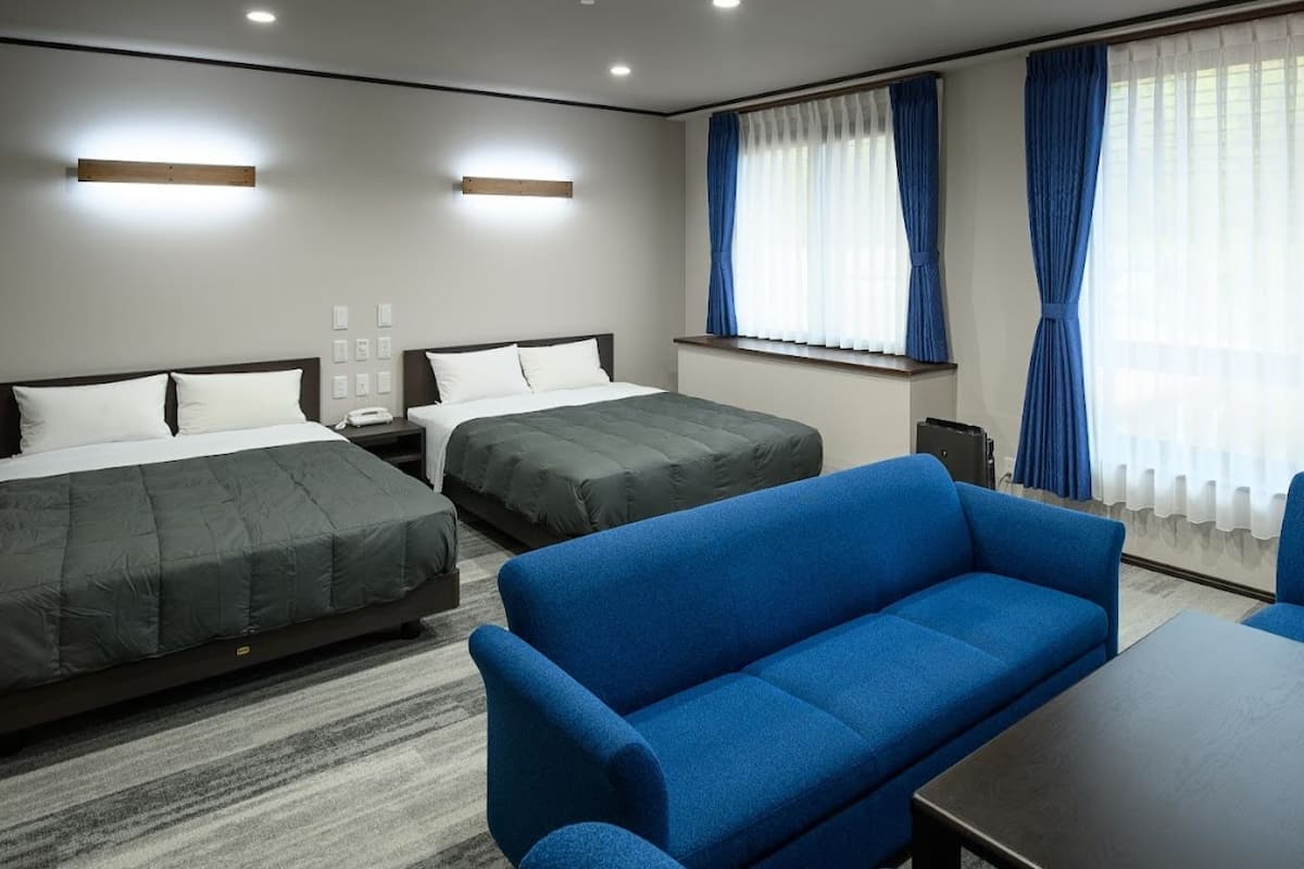 Une chambre d’hôtel avec deux lits, un canapé bleu, une table et une fenêtre avec des rideaux.