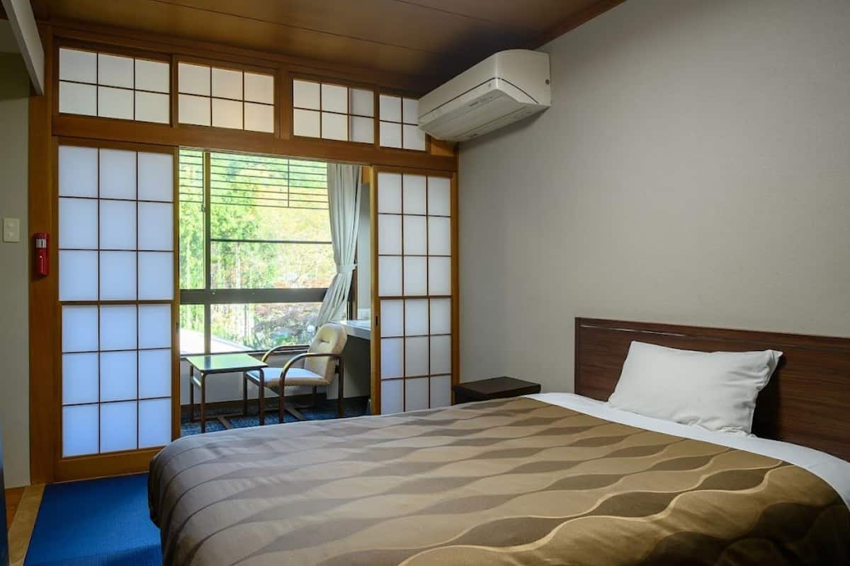 Une chambre d’hôtel équipée d’un lit, d’un bureau, d’une chaise, d’un téléviseur et d’un paravent coulissant de style japonais.