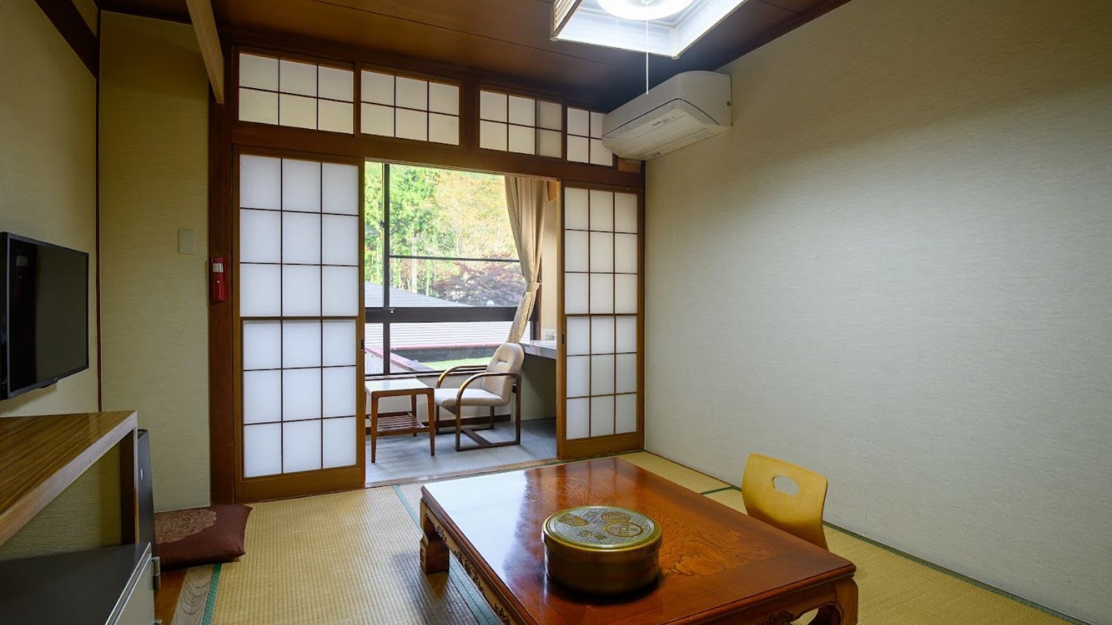 Een traditionele Japanse kamer met tatami vloerbedekking, een houten tafel, een televisie en schuifdeuren.