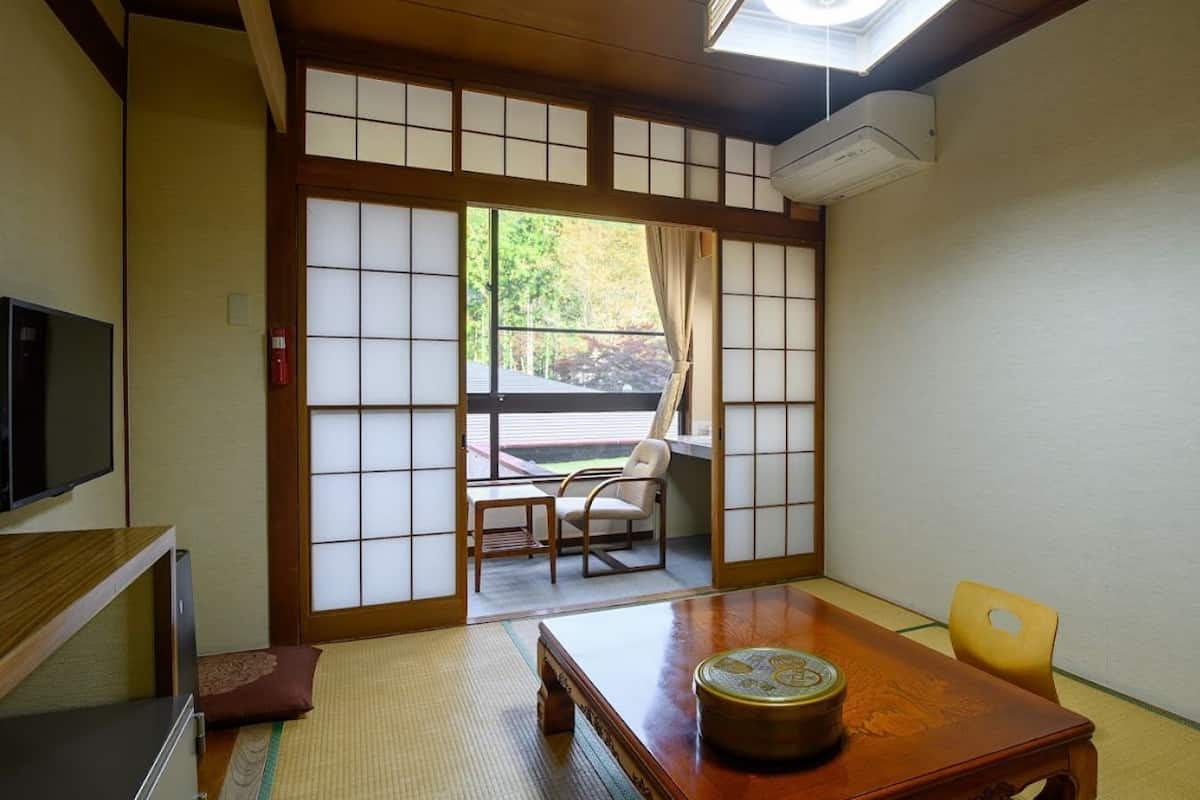 Une pièce de style japonais traditionnel, avec un sol recouvert de tatamis, une table en bois, un téléviseur et des portes coulissantes.