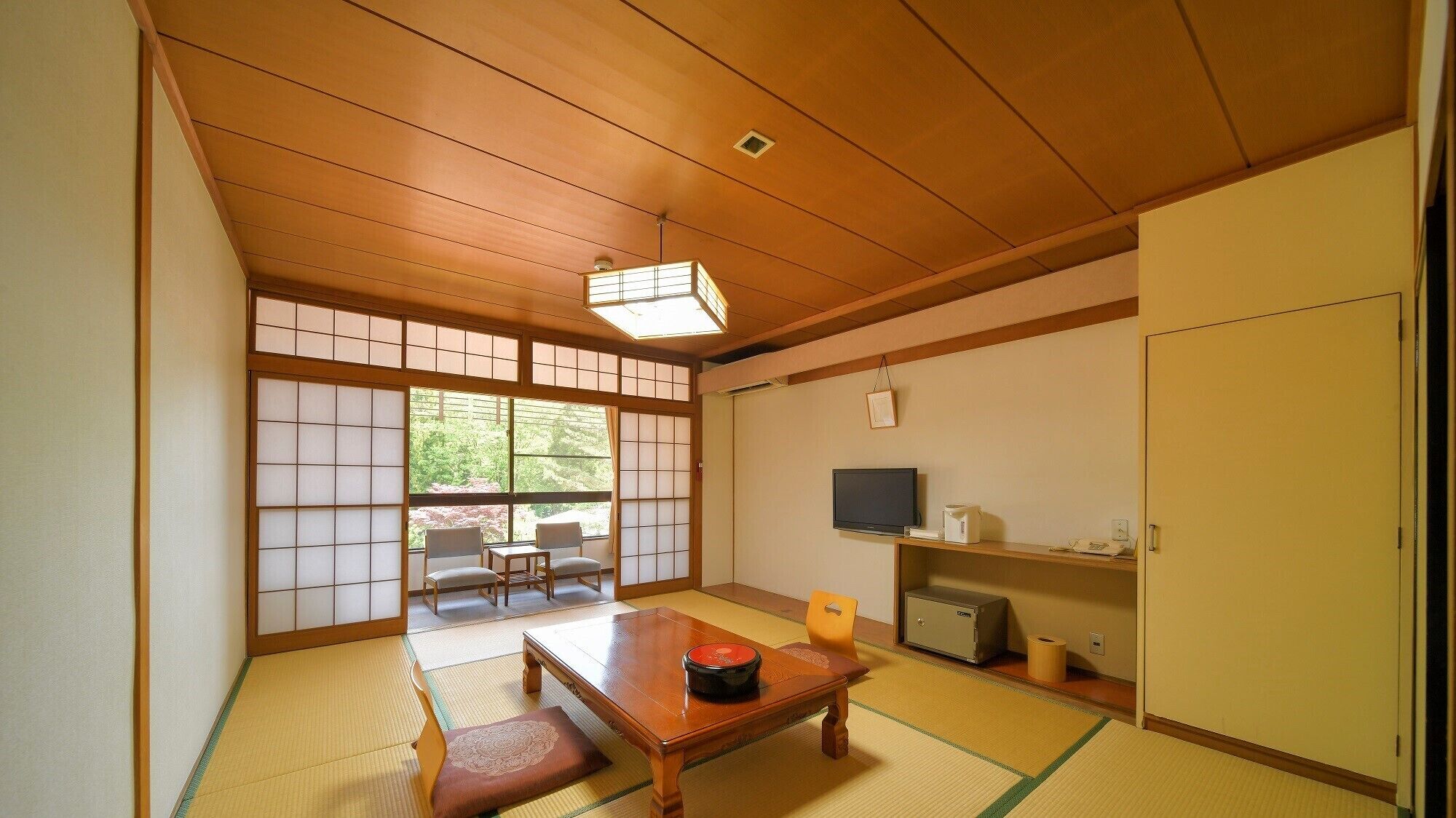 Una habitación japonesa tradicional con suelo de tatami, una mesa baja con un objeto rojo, un televisor y un armario.