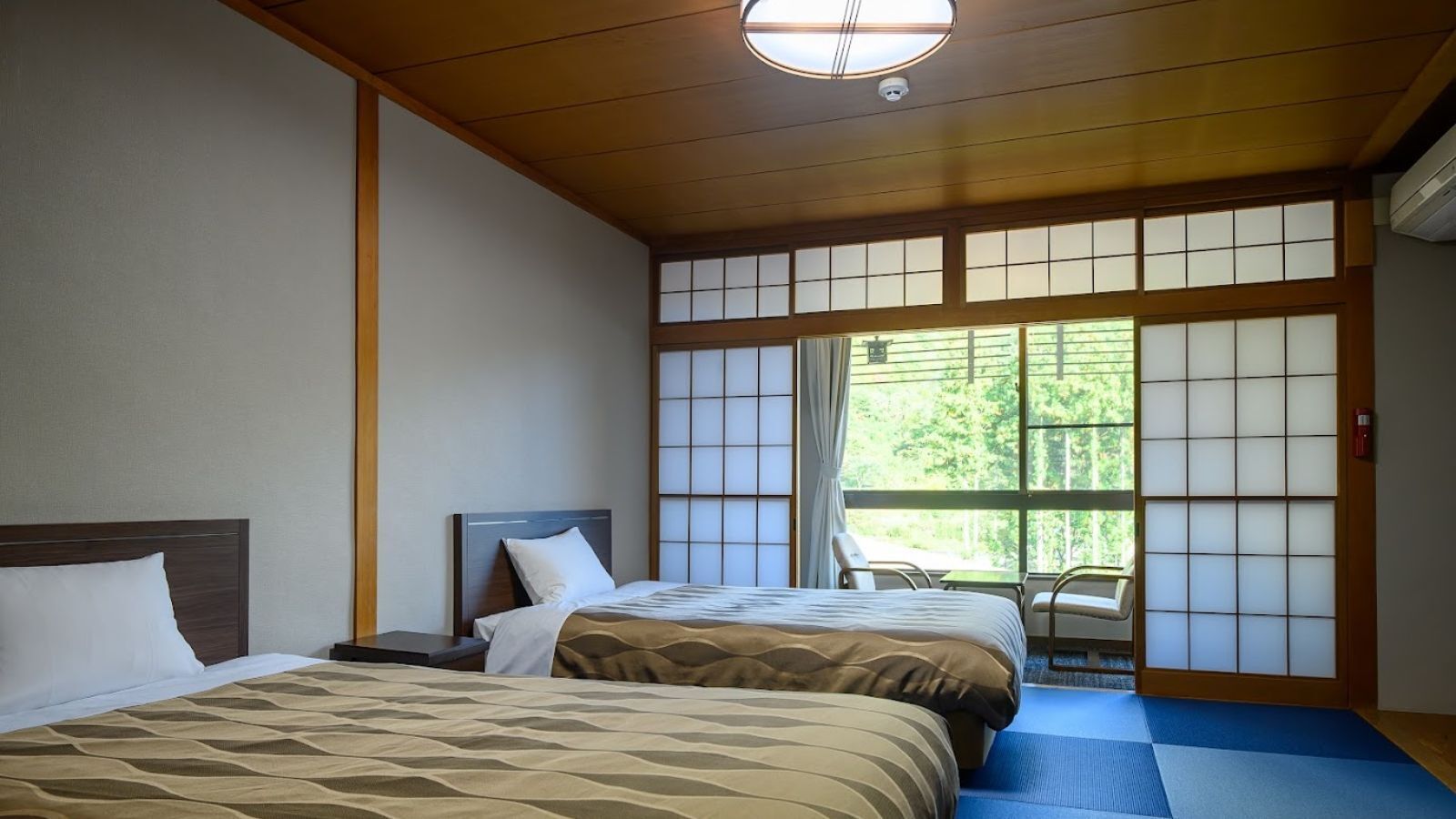 Habitación de hotel con dos camas, vista a zonas verdes a través de amplios ventanales y un tradicional puertas correderas japonesas.