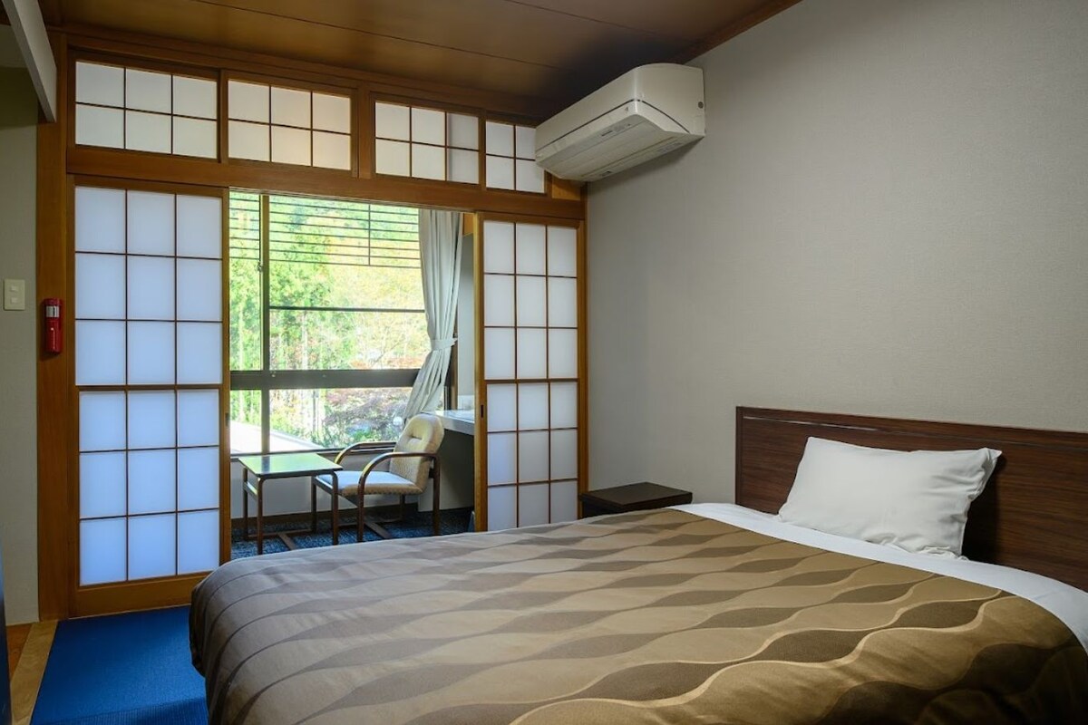 A hotel room with a bed, a desk, a chair, a TV, and a sliding shoji screen.