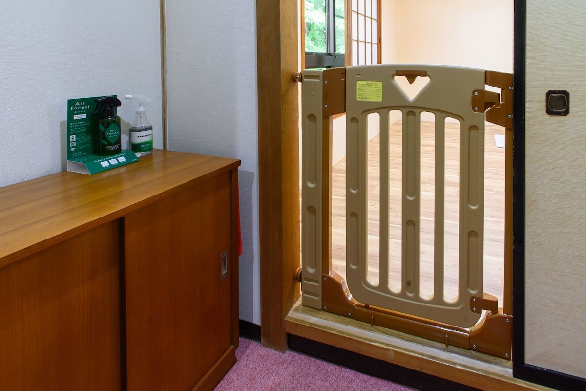 A wooden reception desk with a green informational card, a door with a safety gate, and a window with a view of greenery.