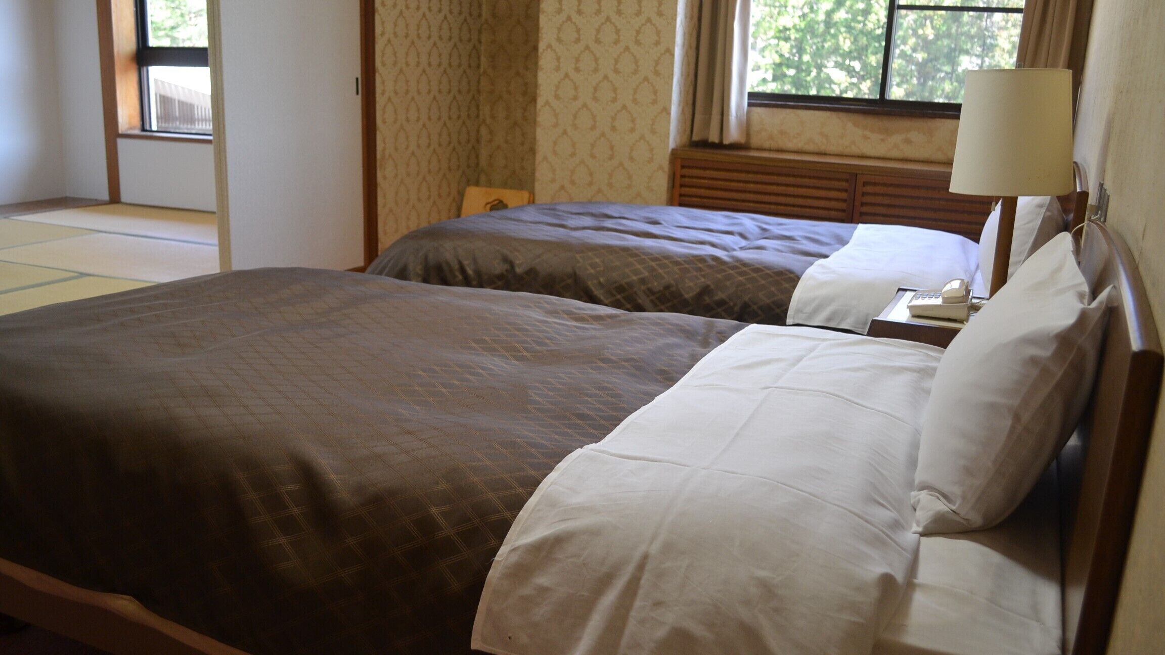 Habitación de hotel con dos camas, una ventana con cortinas, una lámpara de noche y un cabecero de madera.