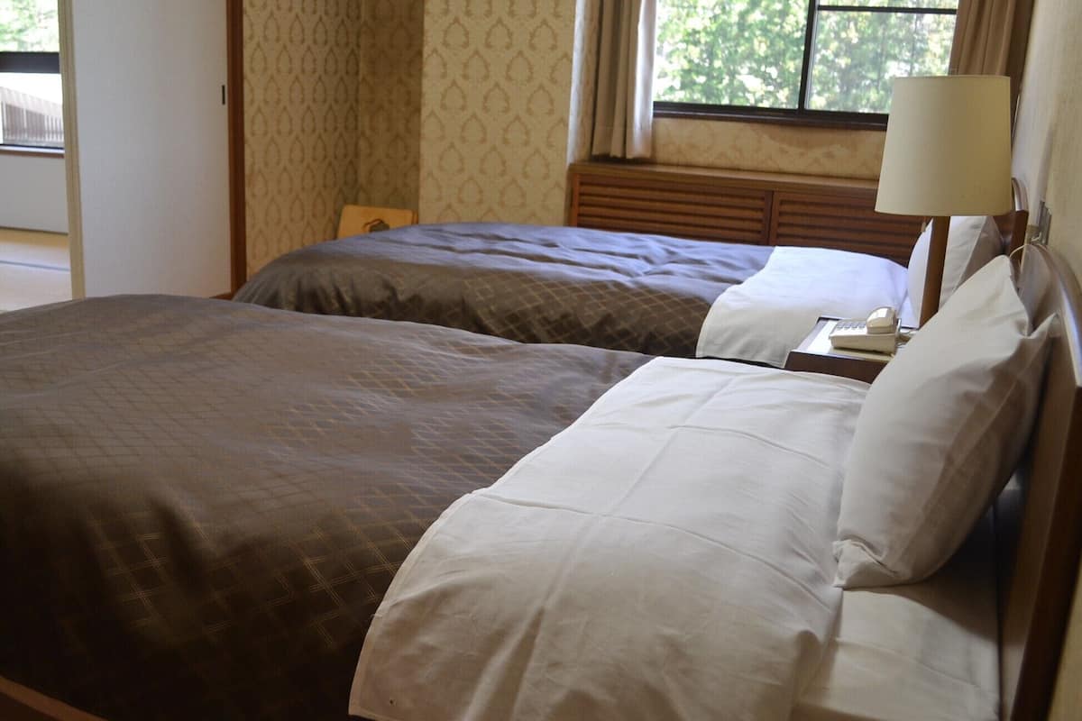 Une chambre d’hôtel avec deux lits, une fenêtre avec des rideaux, une lampe de chevet et une tête de lit en bois.