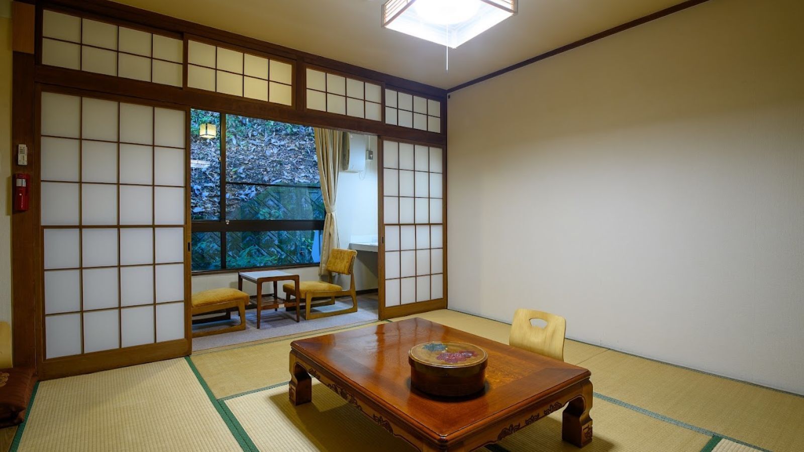 Een traditionele Japanse kamer met tatami vloerbedekking, een lage tafel met decoratieve voorwerpen en schuifdeuren met uitzicht op groen buiten.