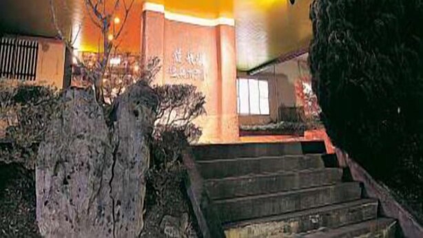 Ein Gebäude mit beleuchteter Beschilderung, einer Treppe zum Eingang und einem gepflegten Garten.