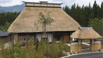 A traditional building with a thatched roof, surrounded by greenery and mountains in the background.