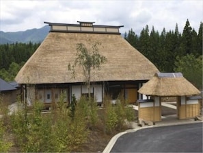 Un edificio tradicional con techo de paja, rodeado de vegetación y montañas al fondo.