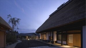 Un edificio de estilo japonés tradicional con techo de paja, un porche de madera y un sendero que lleva a la entrada.