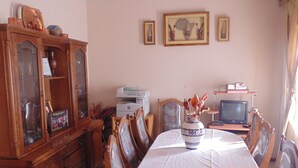 A dining room with a large wooden table, chairs, a cabinet with glass doors, a television, and framed pictures on the wall. - TDJ's B&B (Soweto)