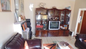 A living room with a brown leather sofa, a television, and a cabinet with glass doors. - TDJ's B&B (Soweto)
