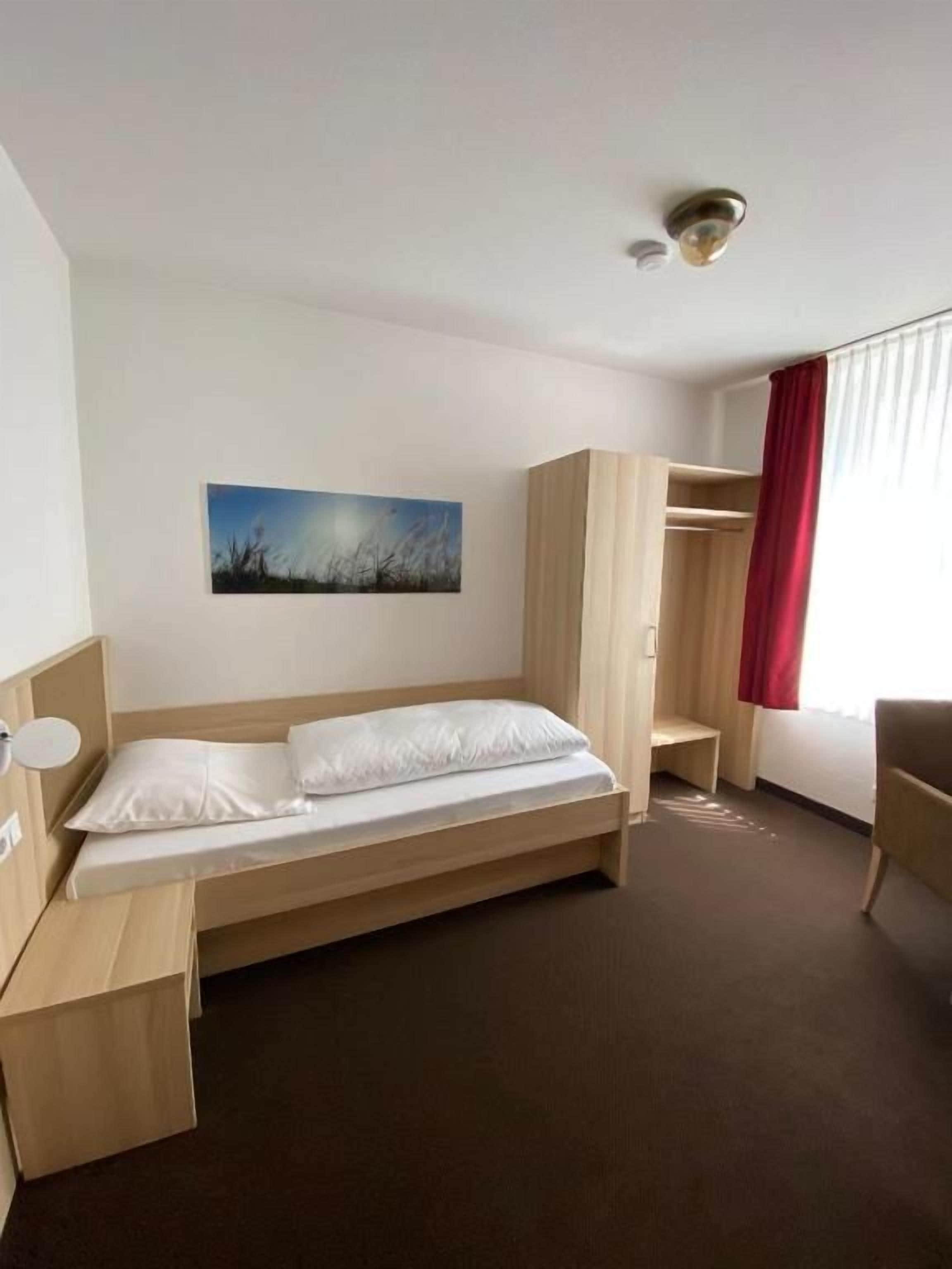 Una habitación de hotel con cama, escritorio, silla, armario y un cuadro en la pared.