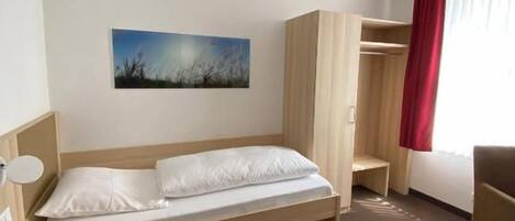 Una habitación de hotel con cama, escritorio, silla, armario y un cuadro en la pared.