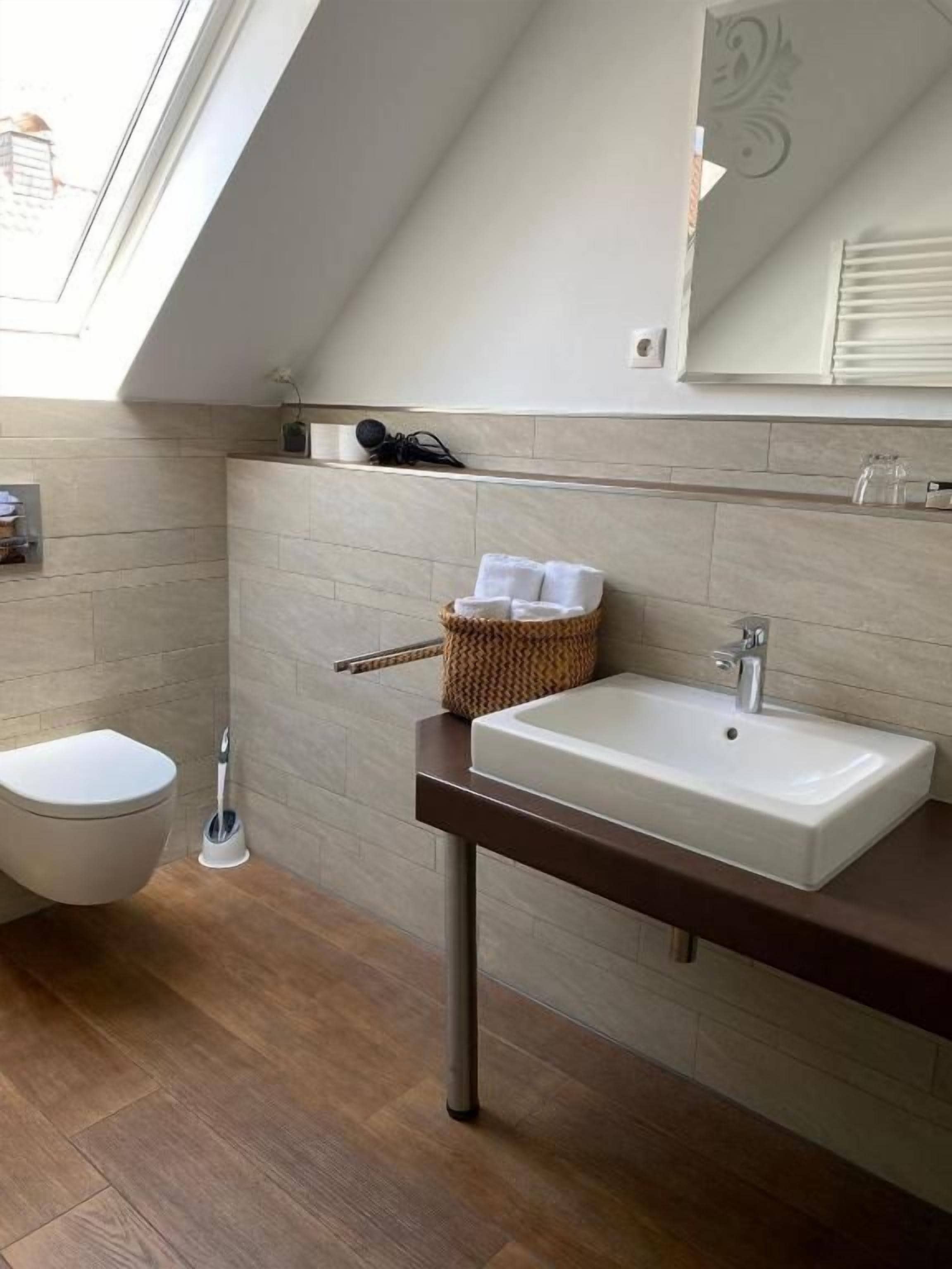 Un baño moderno con tragaluz, inodoro blanco, suelo de madera, lavabo blanco y espejo.