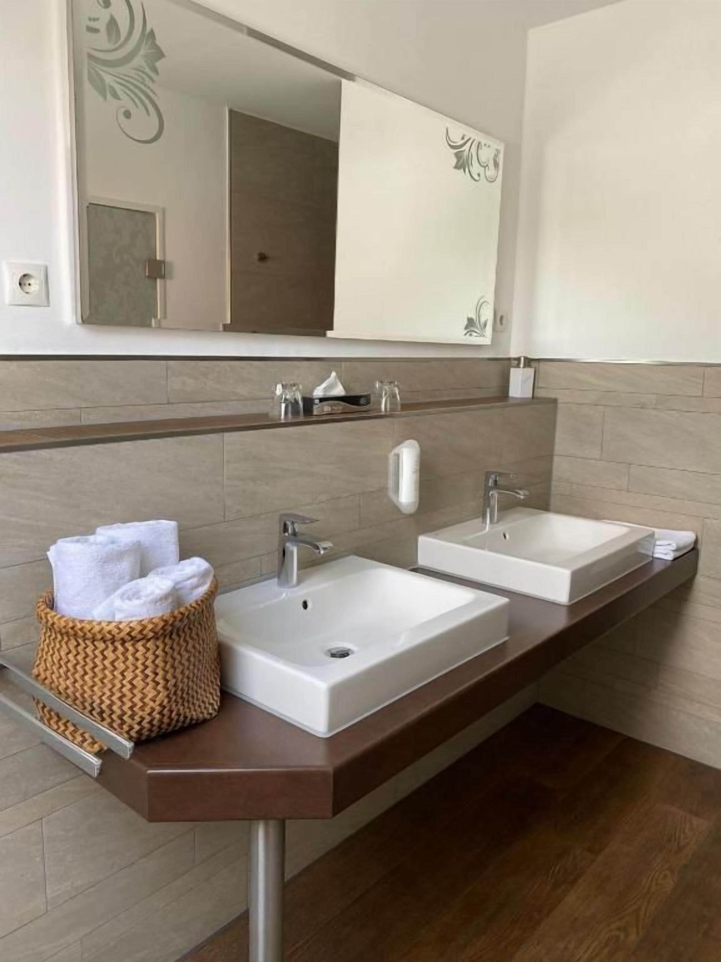 Un baño con dos lavamanos, un espejo y un cesto para toallas.