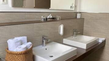 Un baño con dos lavamanos, un espejo y un cesto para toallas.