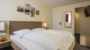 A hotel room with two beds, a bedside table with fruit, a TV, and a mirror. - Hotel Alt Westerholt (Herten)