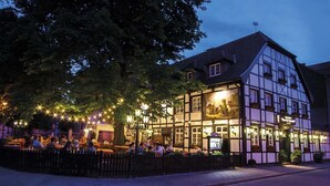 A traditional European building with a pub area, outdoor seating, and a large tree providing shade. - Hotel Alt Westerholt (Herten)