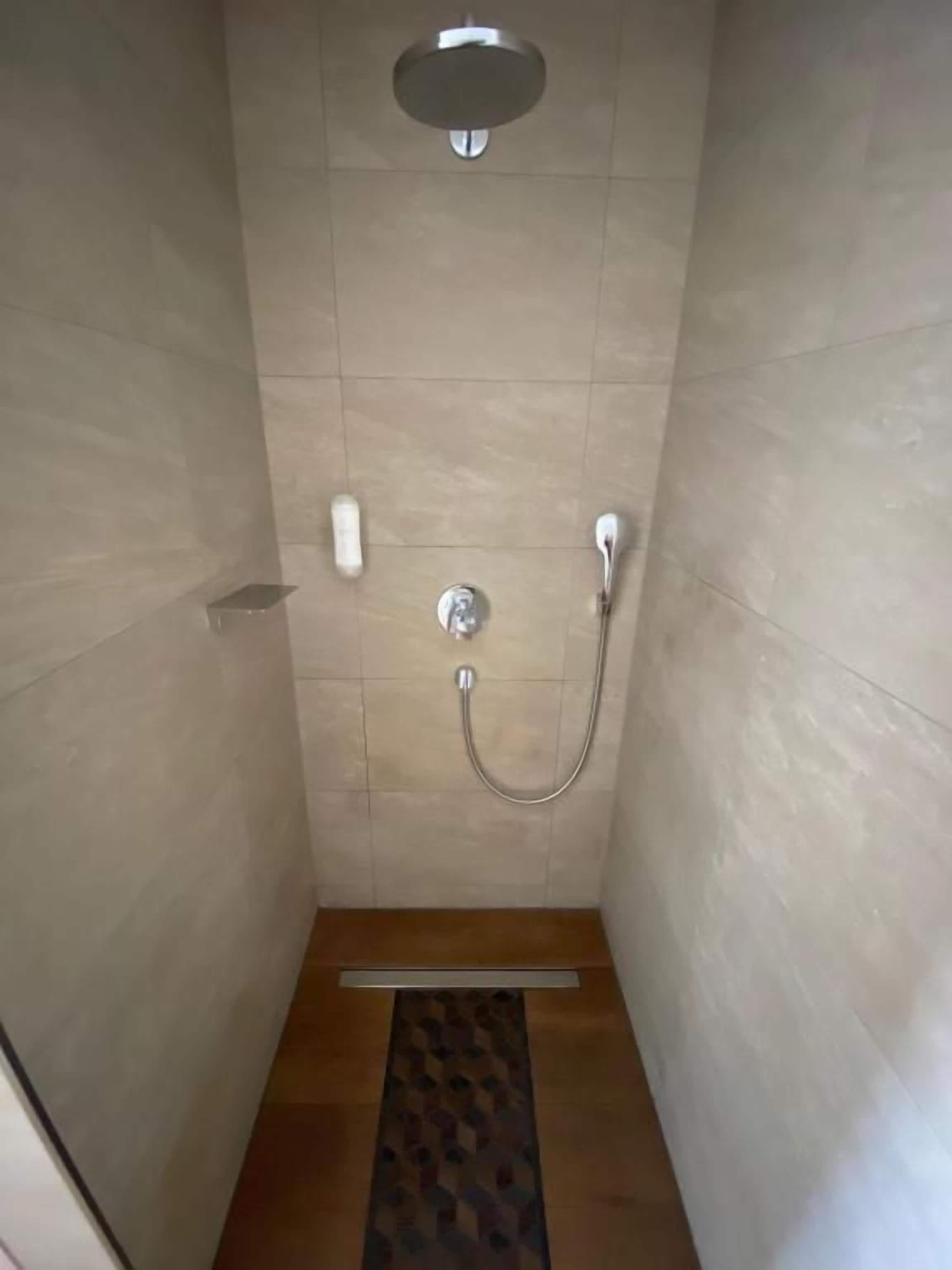 A small, enclosed shower area with a showerhead, a handheld showerhead, and a floor drain.