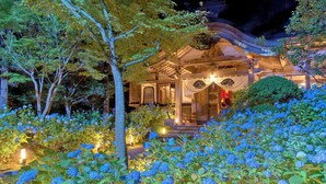 Un bâtiment de style japonais traditionnel, à la structure en bois, entouré d’une végétation luxuriante et de fleurs d’hortensias bleues.