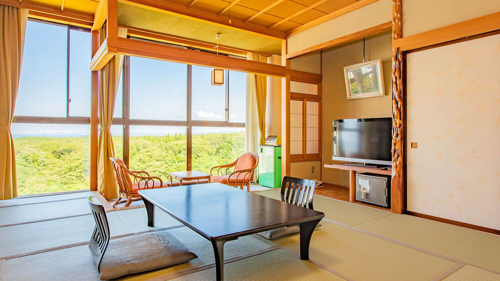 Una habitación con suelo de tatami, una mesa, sillas, un televisor y vistas a zonas verdes.