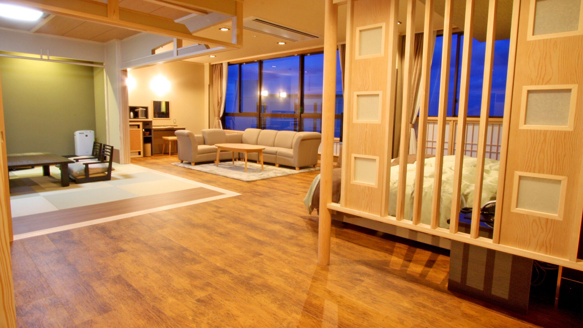 Una habitación con suelo de madera, un sofá, una mesa de centro, una mesa de comedor con sillas, una zona de cocina y un ventanal con vistas.