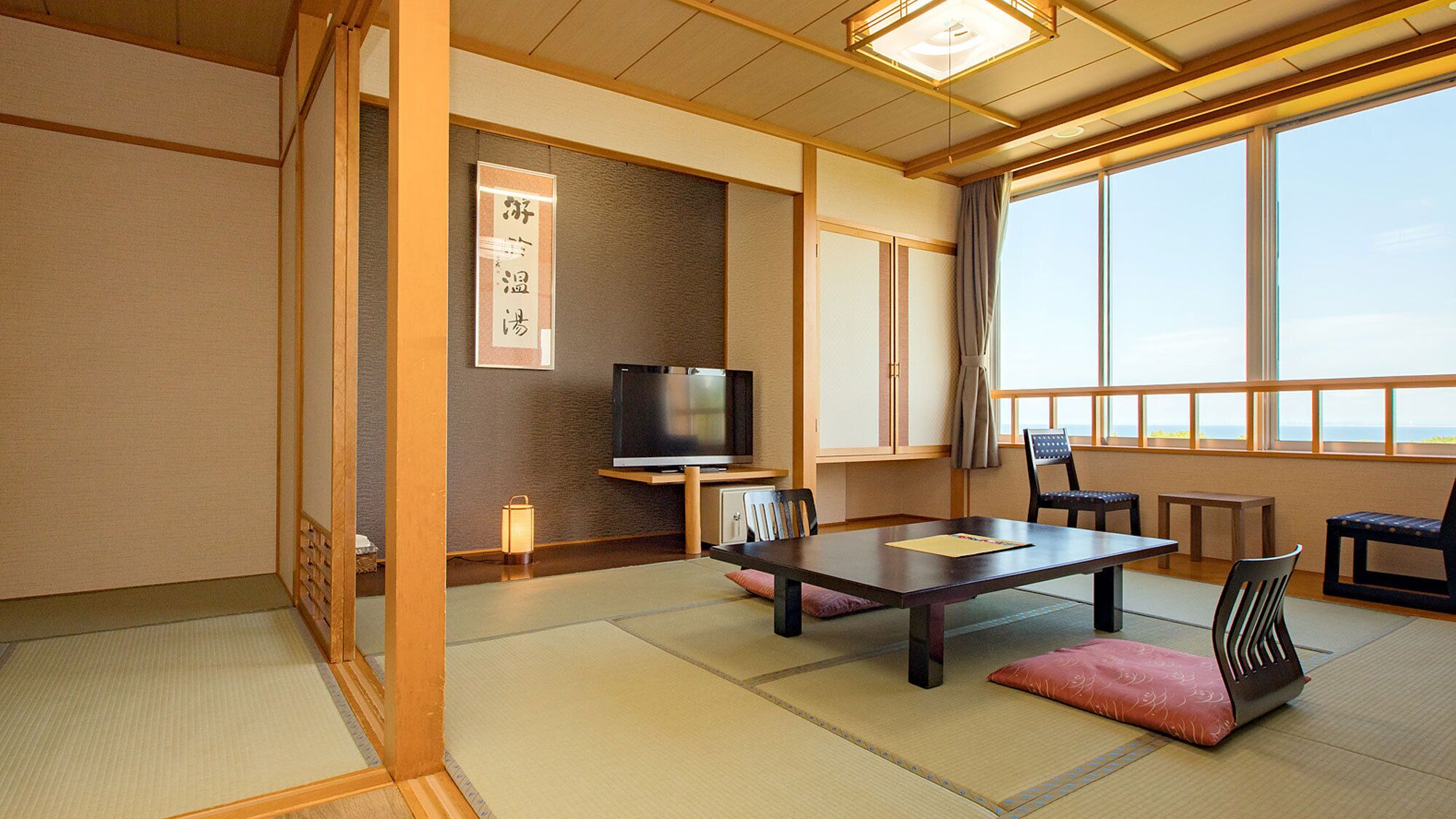 Una habitación japonesa tradicional con suelo de tatami, televisión, mesa, sillas y un ventanal con vistas.