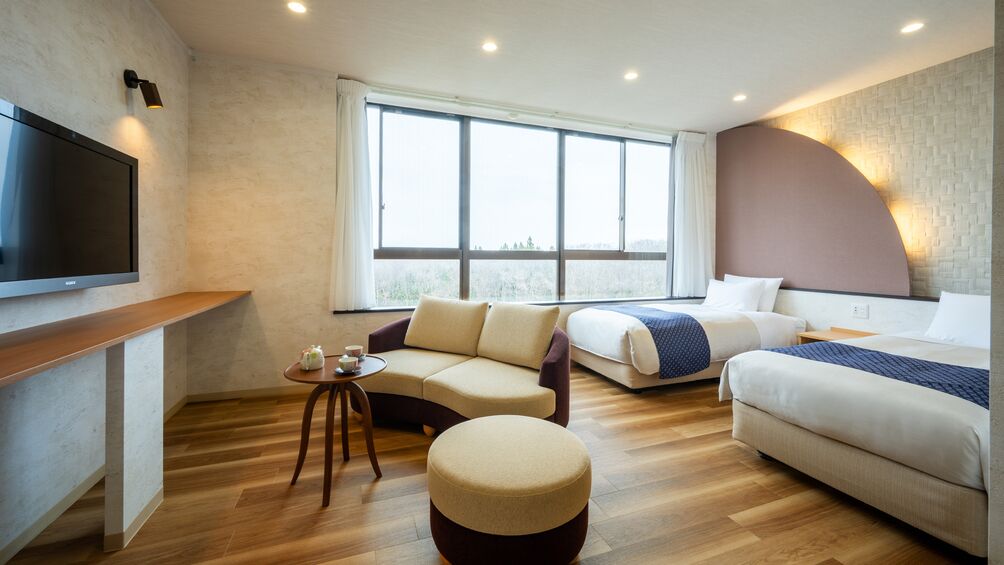 Una habitación de hotel moderna con un ventanal grande, un sofá, una cama, un televisor y una mesita.