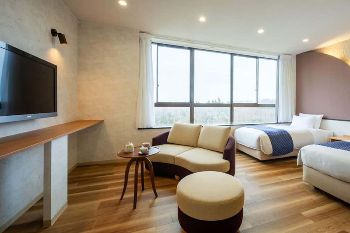 Moderni hotellihuone, jossa on suuri ikkuna, sohva, sänky, televisio ja pieni pöytä.