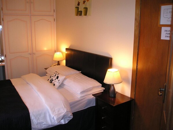 A neatly made bed with white linens and a floral pillow, flanked by two bedside lamps. - Mountain View Guesthouse (Oughterard)