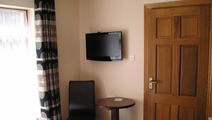 A room with a bed, a chair, a small table, a television mounted on the wall, and a wooden door. - Mountain View Guesthouse (Oughterard)