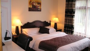 A hotel room with a large bed, two bedside lamps, a painting on the wall, and a window with curtains. - Mountain View Guesthouse (Oughterard)
