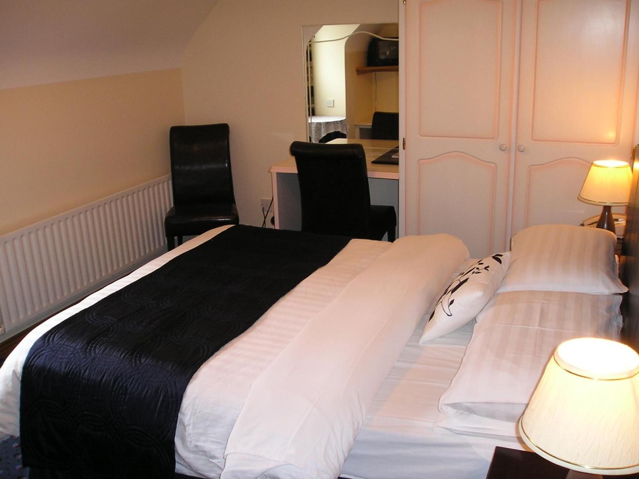 A hotel room with a bed, a desk, a chair, and a lamp.