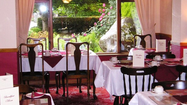 A restaurant with tables set for breakfast, a menu sign, and a view of a garden through the window. - Mountain View Guesthouse (Oughterard)