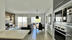 Een moderne keuken met een groot schiereiland, een ingebouwde oven en een eethoek met een tafel en stoelen.
