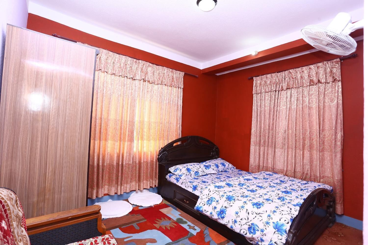 Une chambre à coucher avec un lit, des rideaux, un ventilateur et un tapis à motifs.