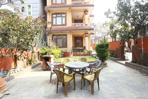 A two-story building with a balcony, a garden with potted plants, and a round table with chairs in the foreground. - Kantipur Temple Homestay (Tarakeshwar)