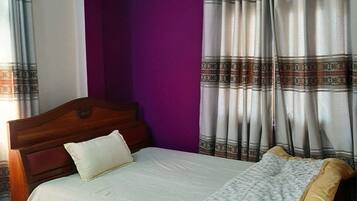A bedroom with a wooden bed, purple walls, patterned curtains, and a colorful rug.