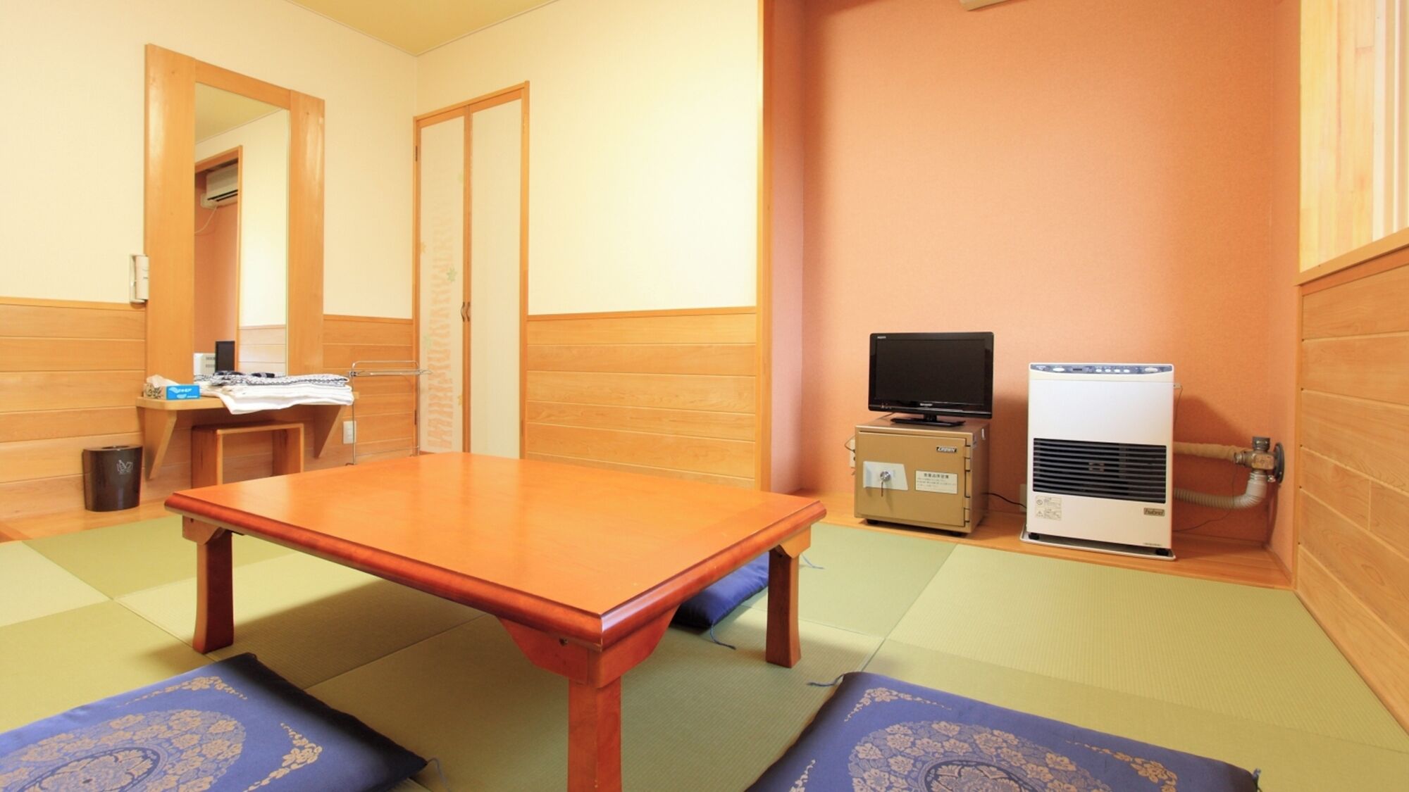 Une pièce avec une table en bois, des tatamis, un téléviseur et un petit climatiseur.