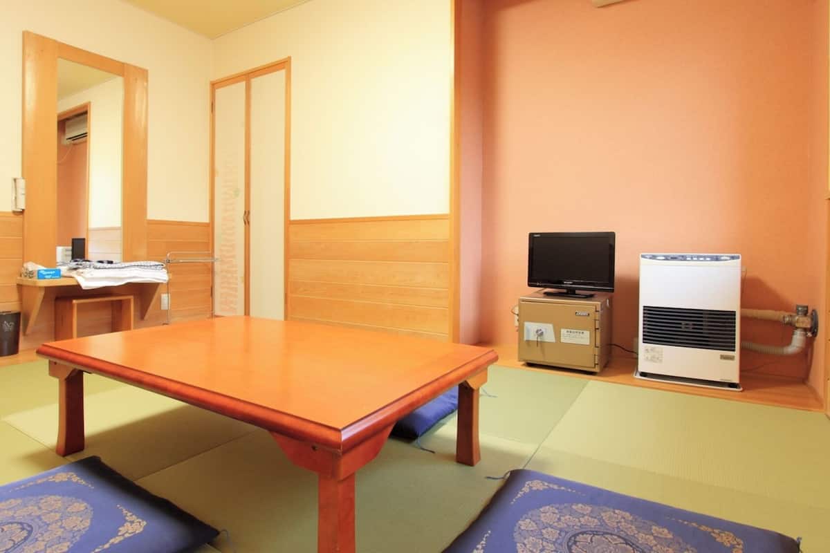 Una habitación con una mesa de madera, esteras de tatami, un televisor y un pequeño aire acondicionado.