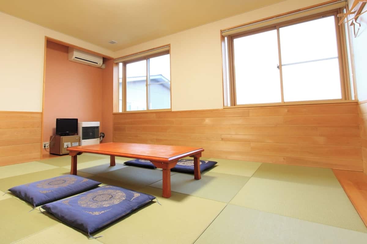 Una habitación con esteras de tatami, una mesa de madera, un televisor y un equipo de aire acondicionado.