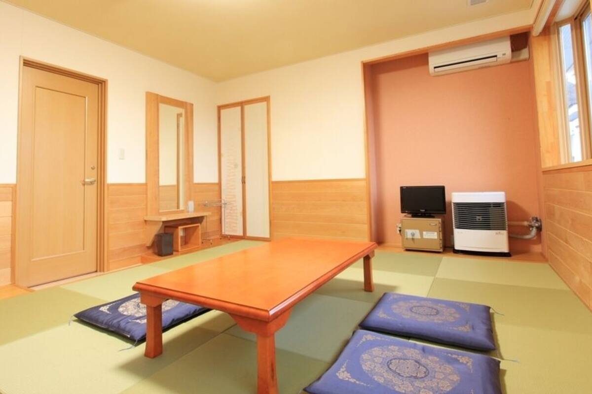 Una habitación con piso de madera, una mesa, un televisor y un aire acondicionado.