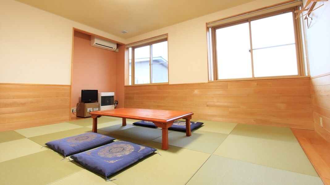 A room with tatami mats, a wooden table, cushions, a television, and a window.