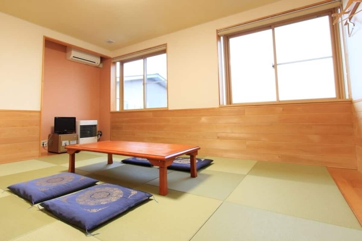 A room with tatami mats, a wooden table, cushions, a television, and a window.